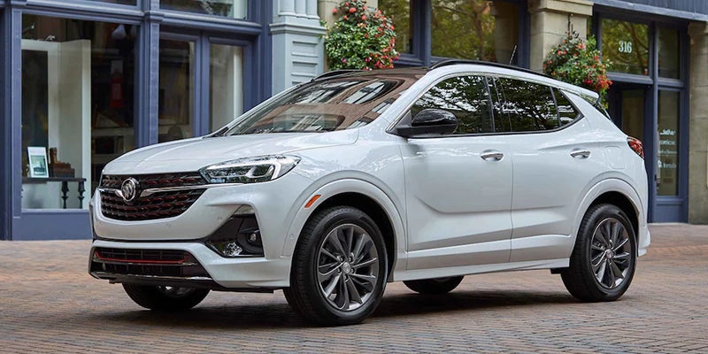 A white Buick Encore GX SUV with a black roof, parked on a cobblestone street in front of a building.