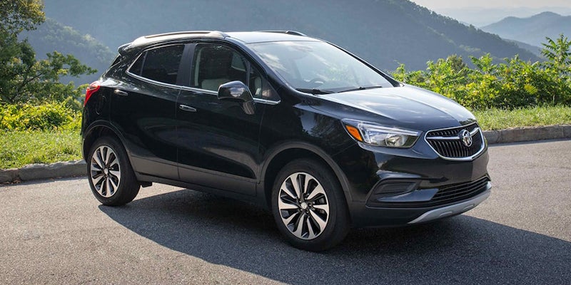 Black Buick Encore SUV parked on asphalt with a blurred mountain and green landscape in the background.