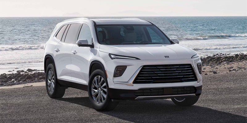 A white SUV with a large front grille parked on an asphalt road beside a rocky beach