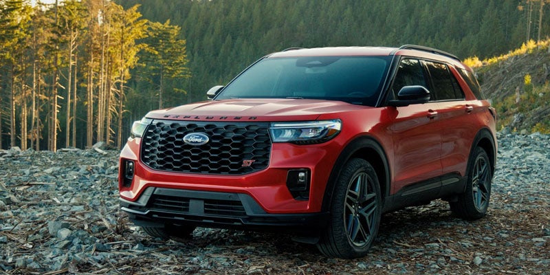 A red Ford Explorer ST SUV parked on a rocky landscape with a forest and sky in the background.