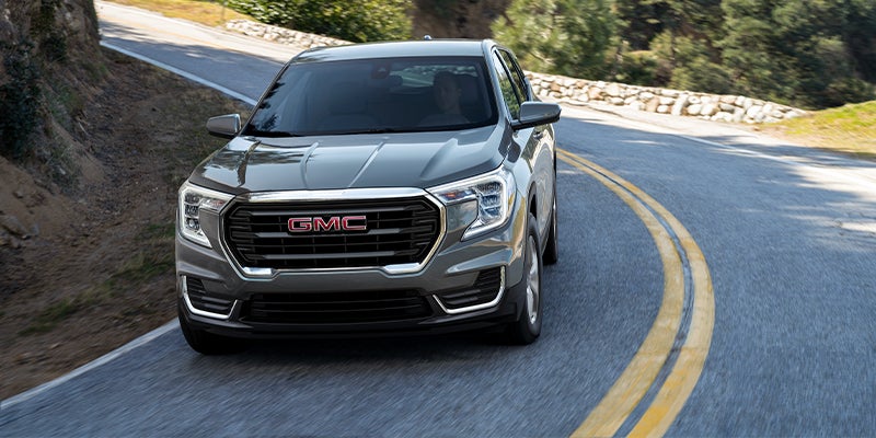 Front view of a dark gray GMC Terrain SUV driving on a two-lane winding road with double yellow lines