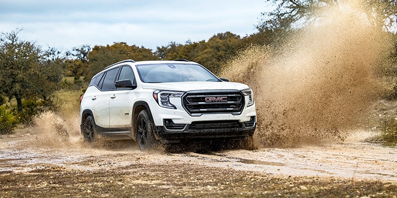 A white GMC Terrain AT4 SUV driving through a muddy puddle