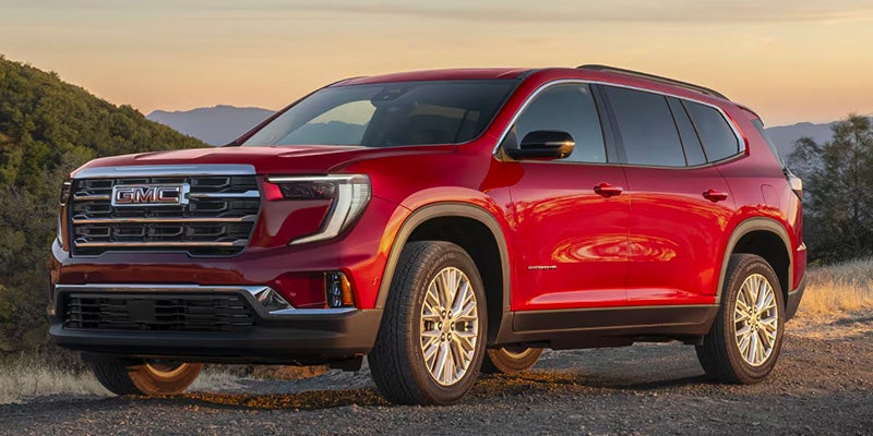 A red GMC Acadia SUV parked on a gravel road at sunset