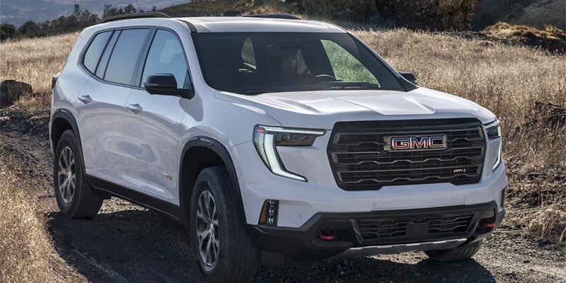 A white GMC Acadia SUV parked on a dirt trail in a dry grassy landscape