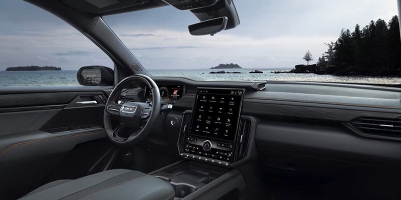 View from driver's seat of modern car, with large infotainment screen and a calm ocean and distant islands.