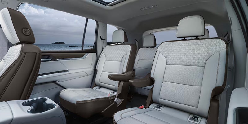 Interior of a vehicle with light gray and brown captain's chairs, showing a view of the ocean through the window.