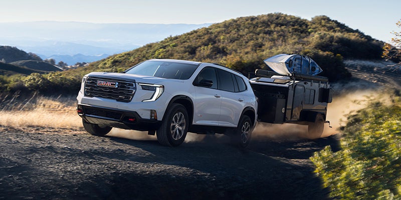 A white GMC Acadia SUV towing an off-road camper trailer along a dusty mountain trail