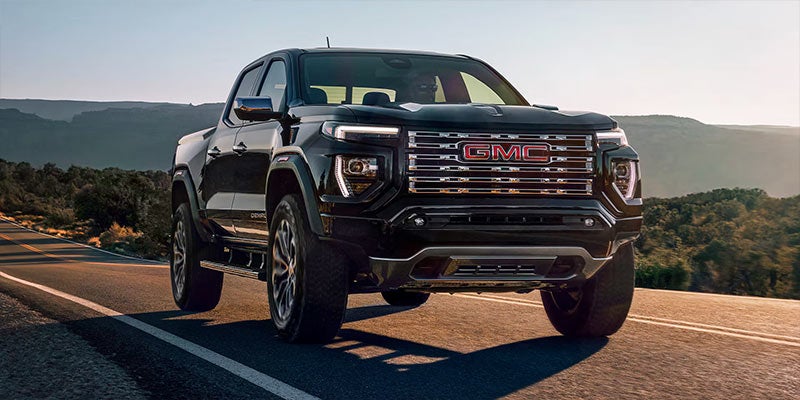 Front view of a black GMC Denali pickup truck with red gmc logo driving on a scenic road