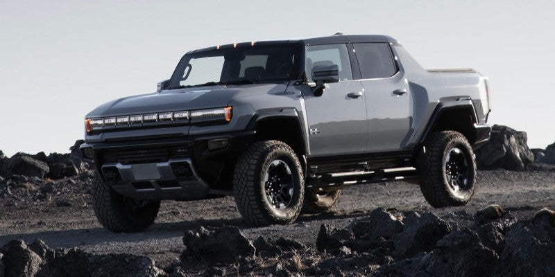 Grey Hummer EV pickup truck driving on a rocky, dark grey terrain under a bright, overcast sky
