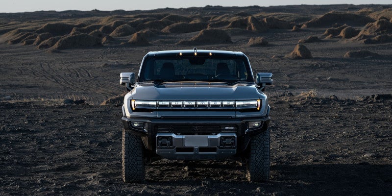 Front view of a dark gray GMC Hummer EV parked on dark, rugged terrain under an overcast sky