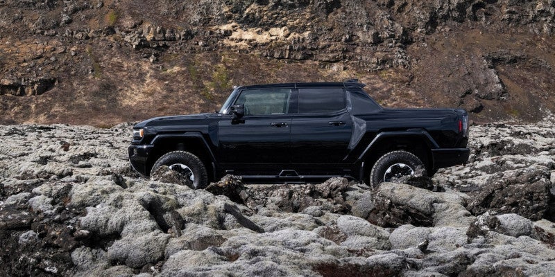 A black Hummer EV truck parked among gray-green mossy rocks