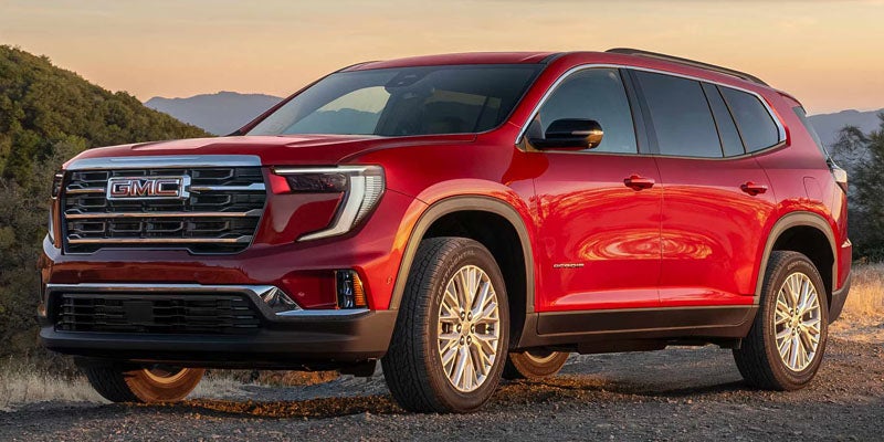 A shiny red GMC SUV parked on a dirt road with green hills