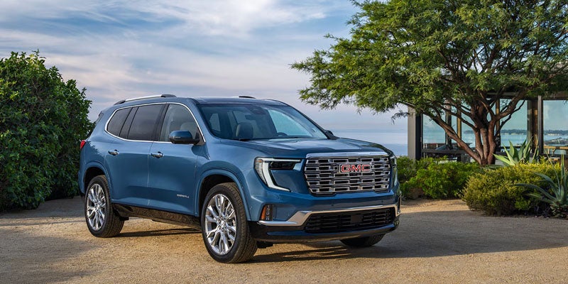 A modern blue GMC Denali SUV parked on a gravel driveway