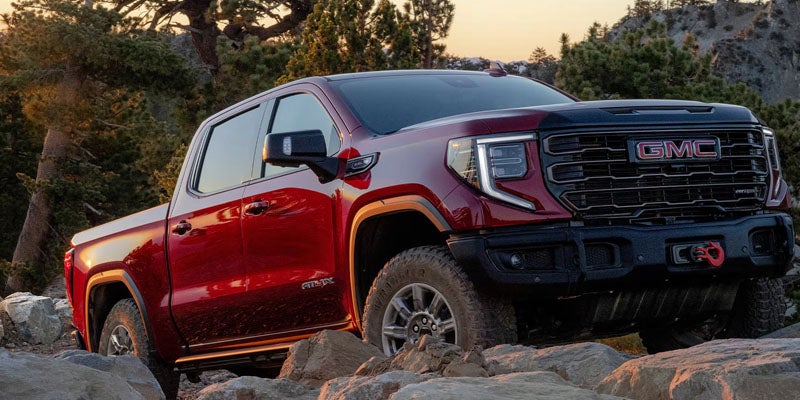 Red GMC Sierra pickup truck with a black grille and front bumper navigates a rocky, off-road terrain