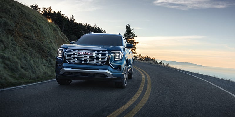 Front view of a dark blue GMC SUV driving on a winding road with a grassy hill to the left