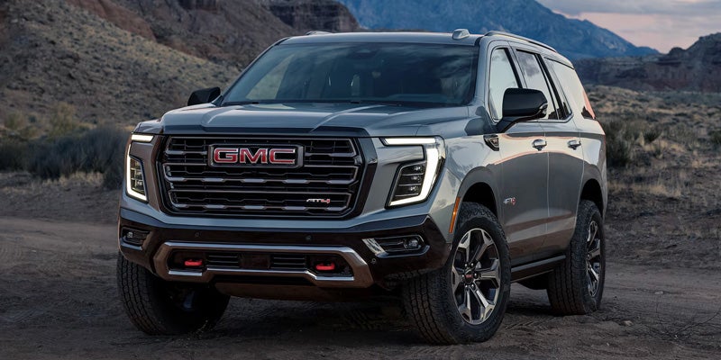 A dark gray GMC Yukon AT4 SUV parked on a dirt road with mountains in the background